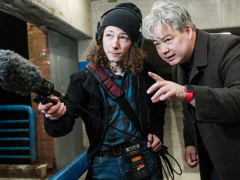 student holds recording equipment in parking garage; male professor instructs